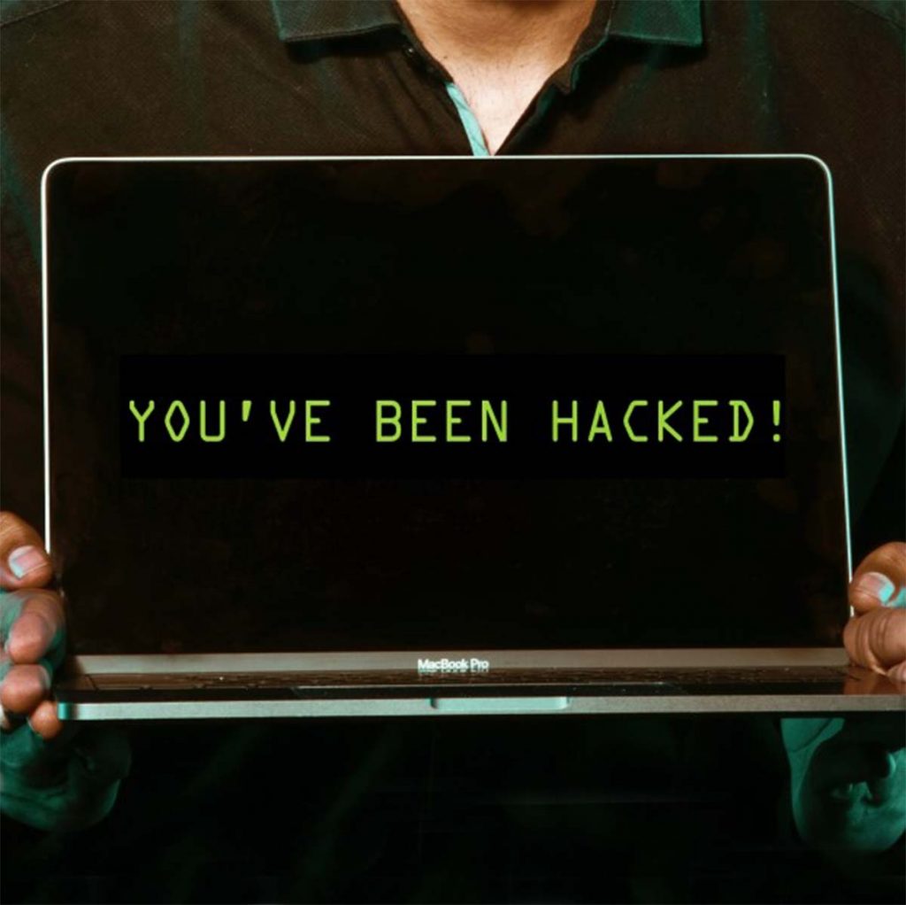 Person zeigt geöffnenten Laptop mit dem Schriftzug "You've been hacked!"