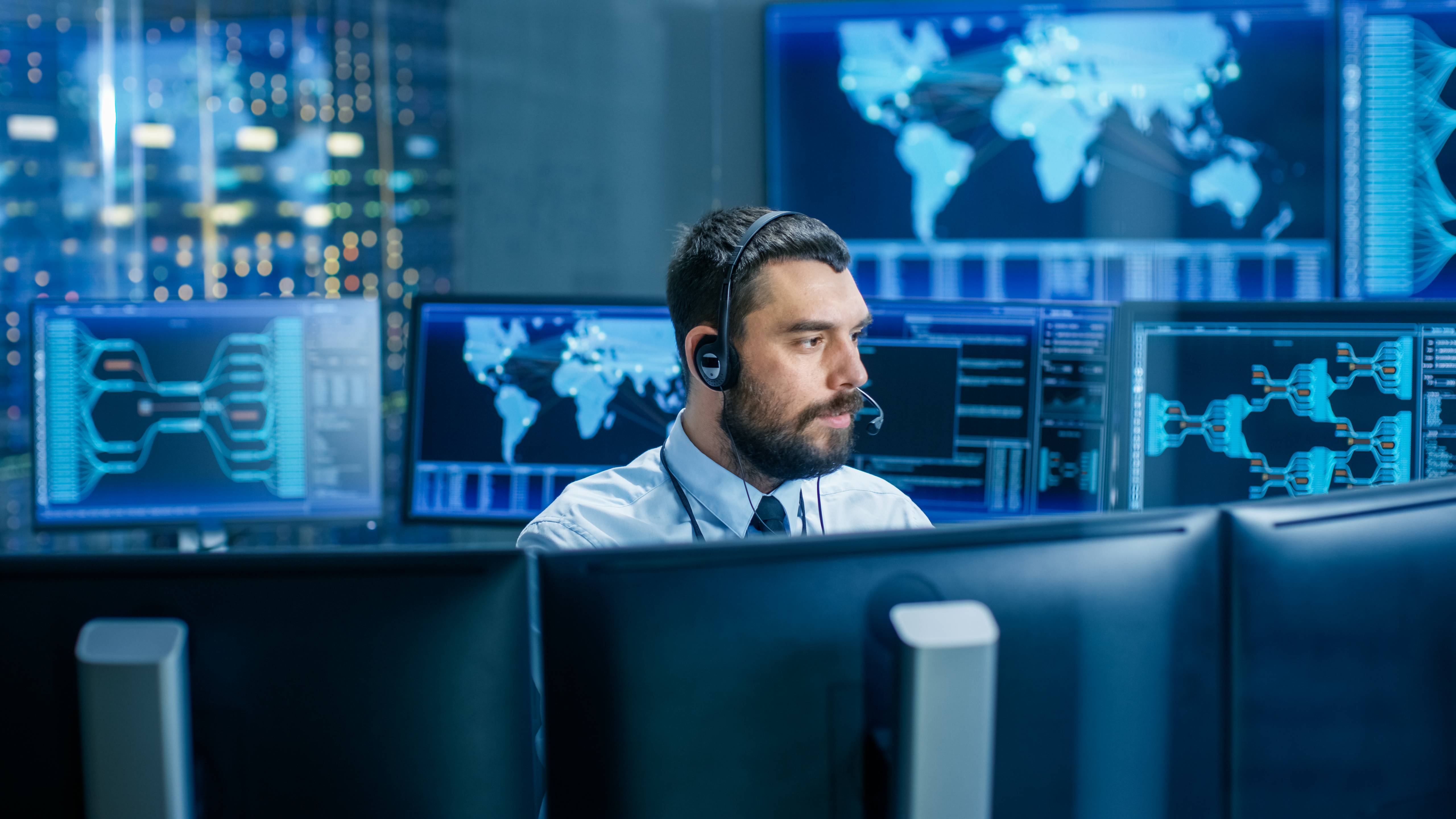 Darum ein SOC von LEITWERK Mann mit Headset sitzt in einem Raum mit vielen Monitoren