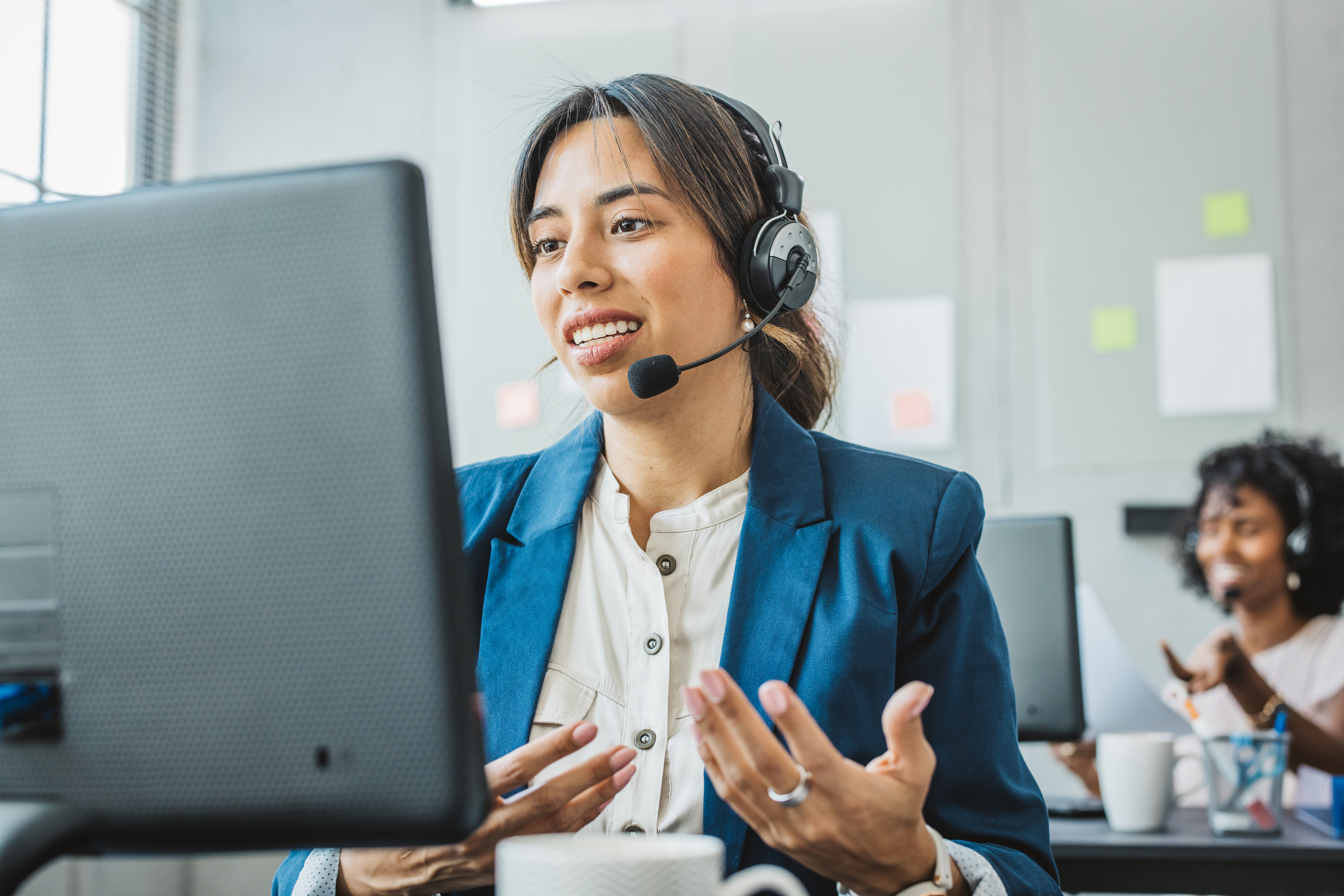 Zwei Personen an einem Arbeitsplatz, vor ihren Monitor mit Headset am artikulieren