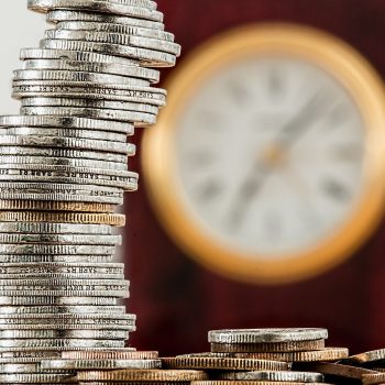 Zeit und Kosten sparen durch IT-Outsourcing gestapeltes Geld mit einer Uhr im HIntergreund