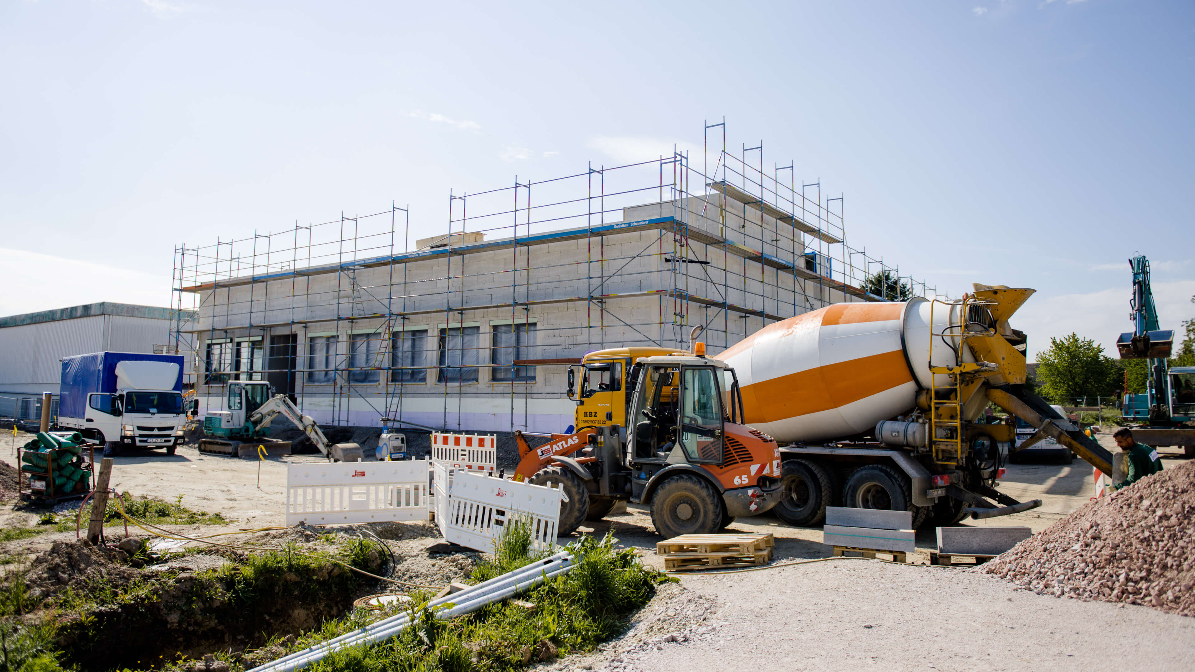 Bild einer Baustelle mit einem Bagger, einem Betonmischer und mehreren Bauzäunen