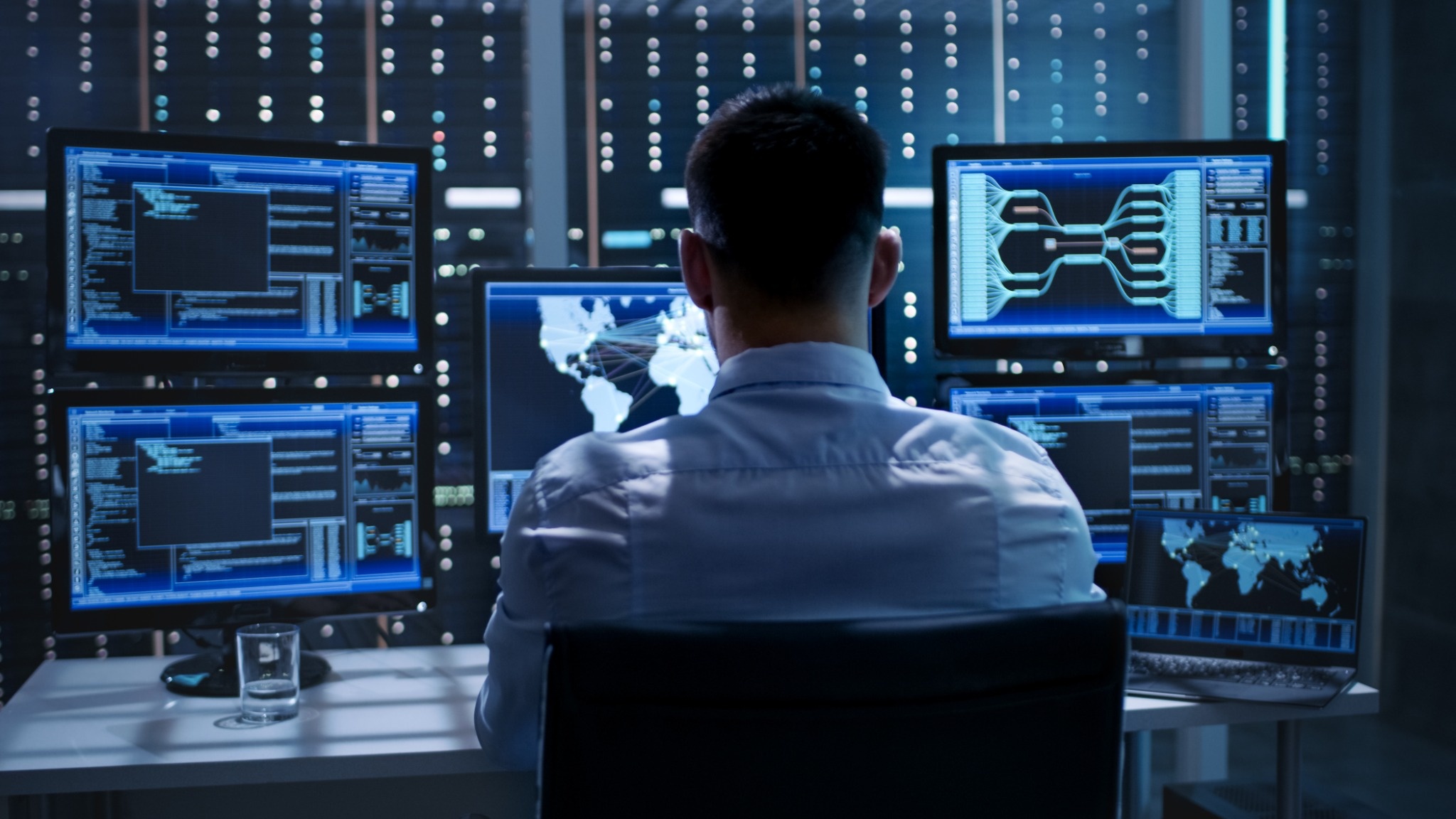 Personen sitzt am Schreibtisch mit fünf Monitoren