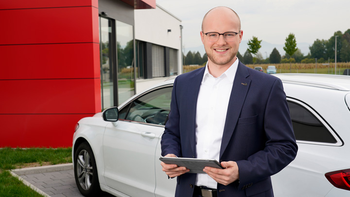 Jobs im Bereich Vertrieb Mitarbeiter mit einem Tablet in der Hand vor einem weißen Auto