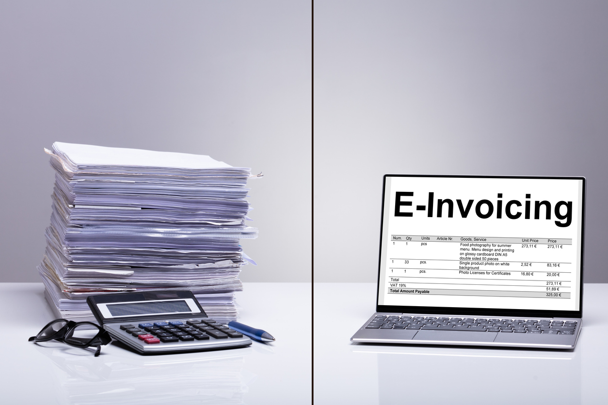 So funktioniert die Übermittlung einer E-Rechnung Ein Stapel voll Papier und daneben im Vergleich ein Laptop mit einer E-Rechnung