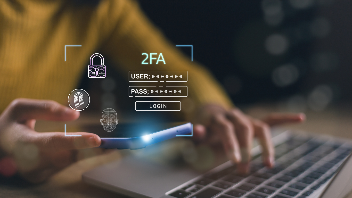 Zwei-Schritte-Authentisierung Person mit Smartphone in der linken Hand und mit der rechten Hand, tippend am Laptop