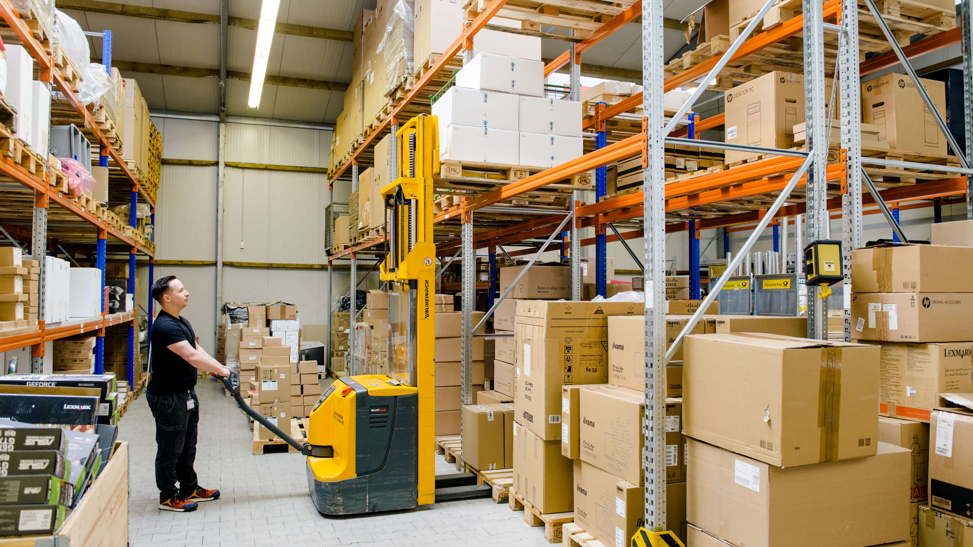 Logistik-Mitarbeiter befördert eine Palette mit einem Hubwagen durch eine Lagerhalle