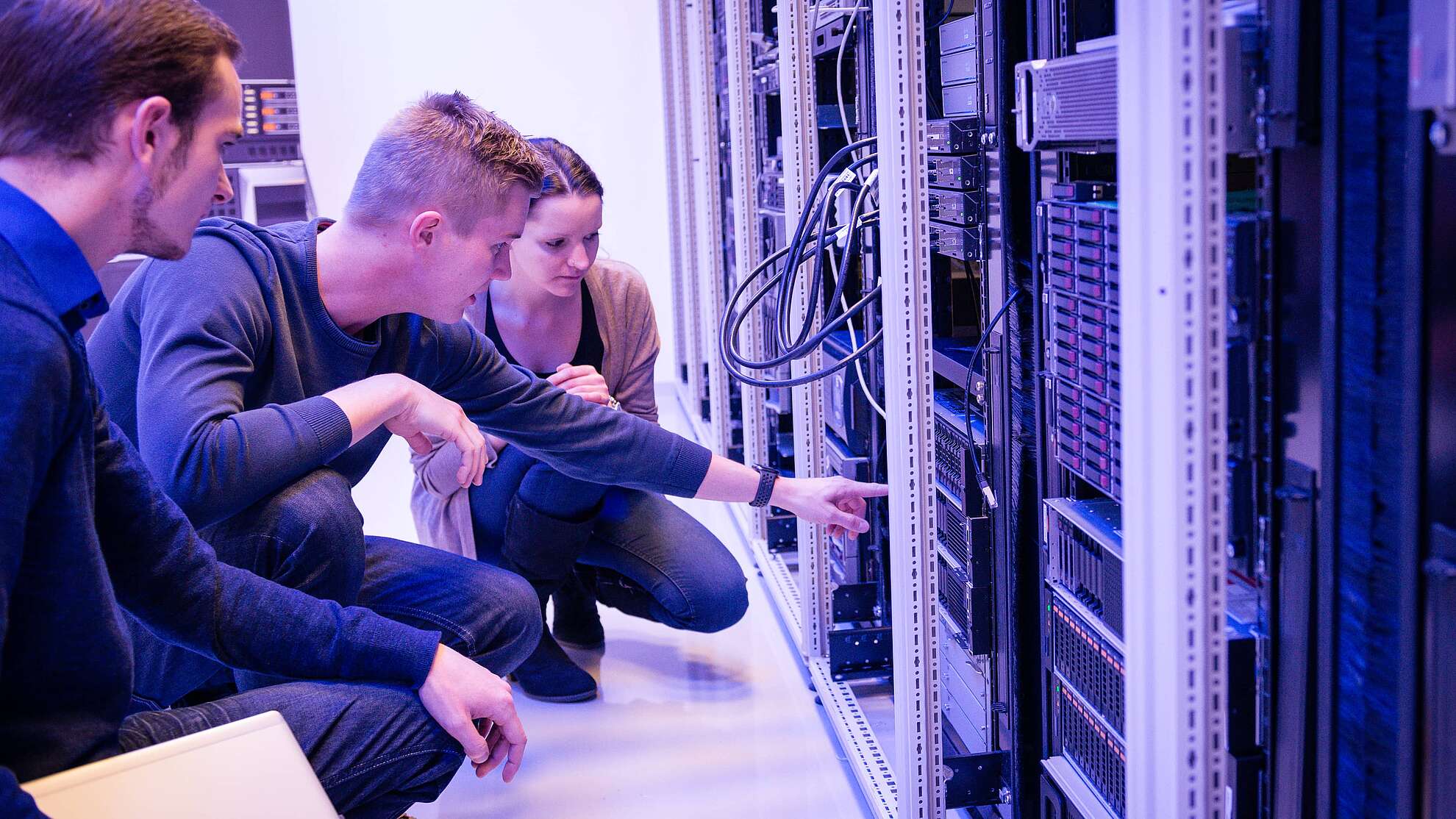 Drei Personen kniend vor einem Serverschrank