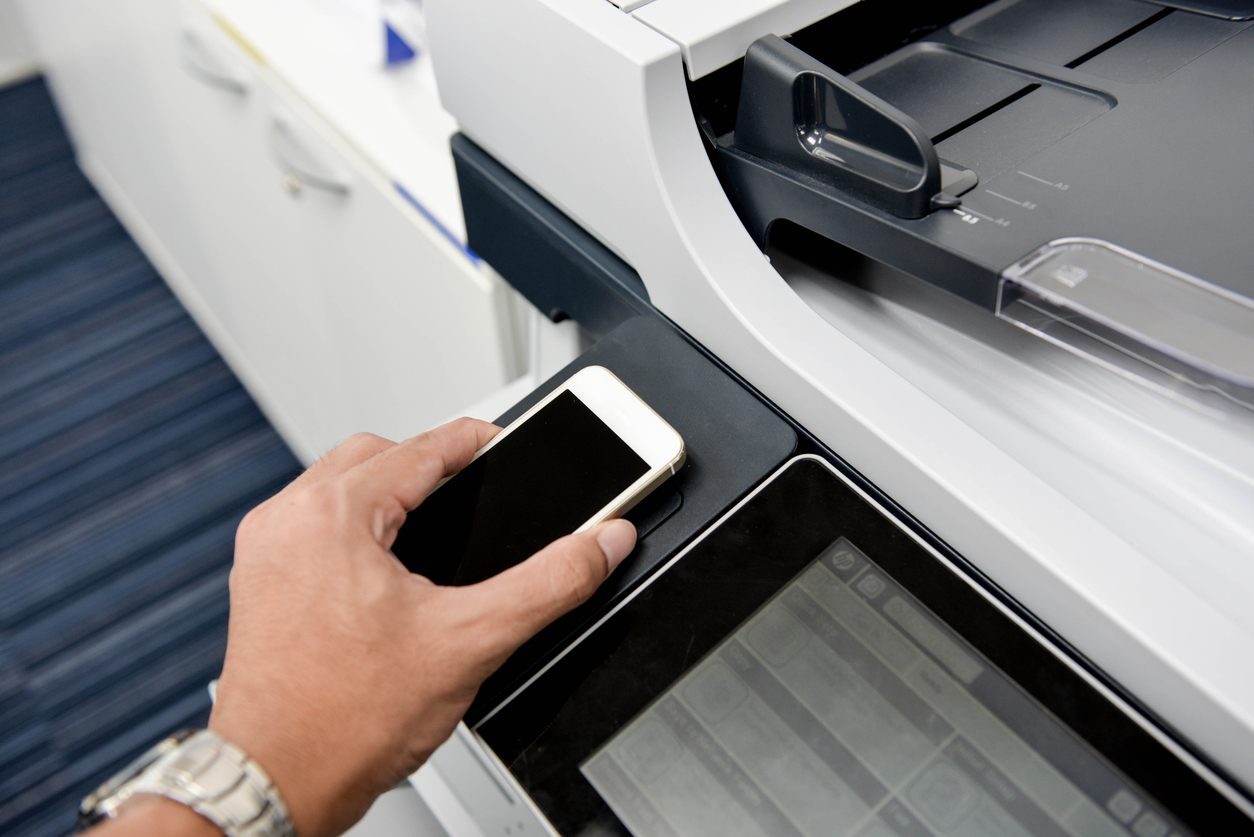 Mitarbeiter hält sein Smartphone an einen Drucker, um sich zu authentifizieren