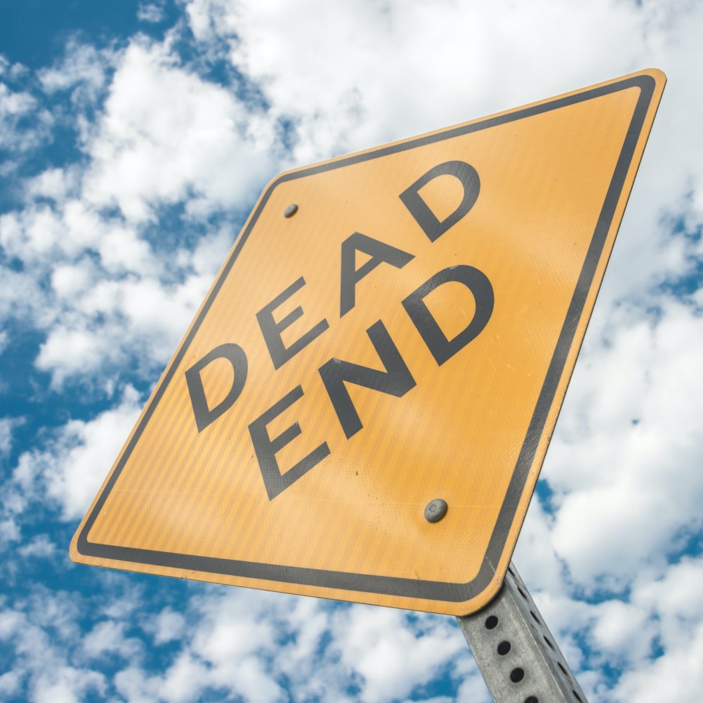 Gelbes Warnschild mit der Aufschrift "Dead End" mit bewölktem Himmel als Hintergrund