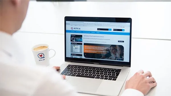 Mann vor einem Notebook mit einer Maus in der Hand und einem Kaffee auf dem Tisch