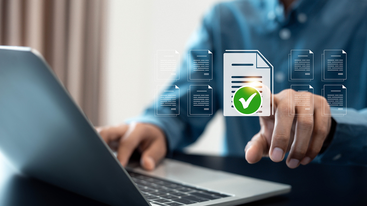 Mann sitzt am Laptop und tippt auf eine digital erscheinende Aufgabe mit einem grünen Haken