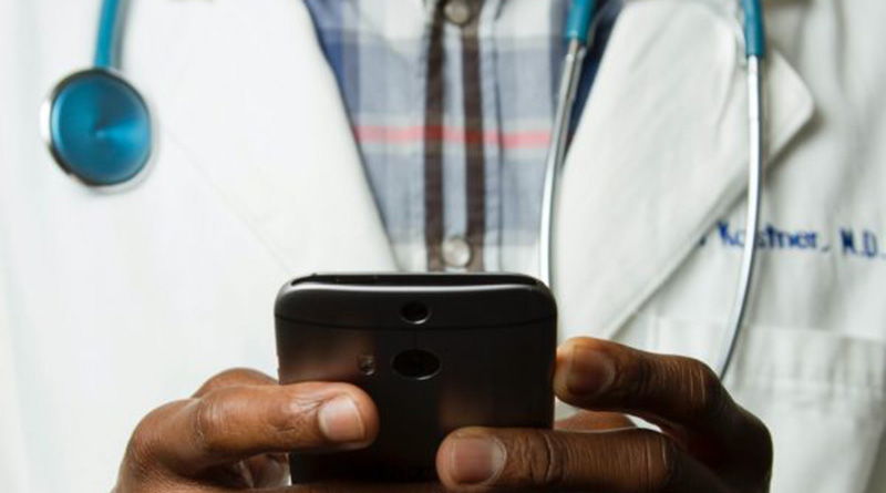 Mann mit Arztkittel hält ein Mobiltelefon