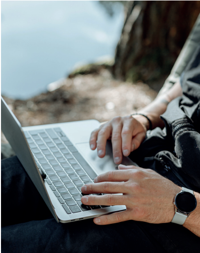 Individuell nutzbares Outdoor WLAN ein Mann sitzt draußen und arbeitet an seinem Laptop. Es sind nur das Laptop auf seinem Schoß und seine Hände zu sehen.