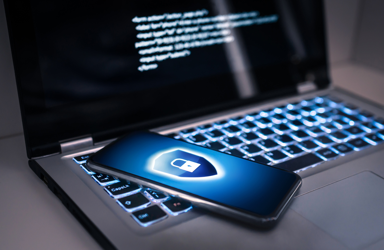 SOC Antivirus Lapot mit beleuchteter Tastatur und unleserliche Codes auf dem Bildschirm. Eine Smartphnone mit Schloss Symbol auf dem Display liegt auf der Tastatur